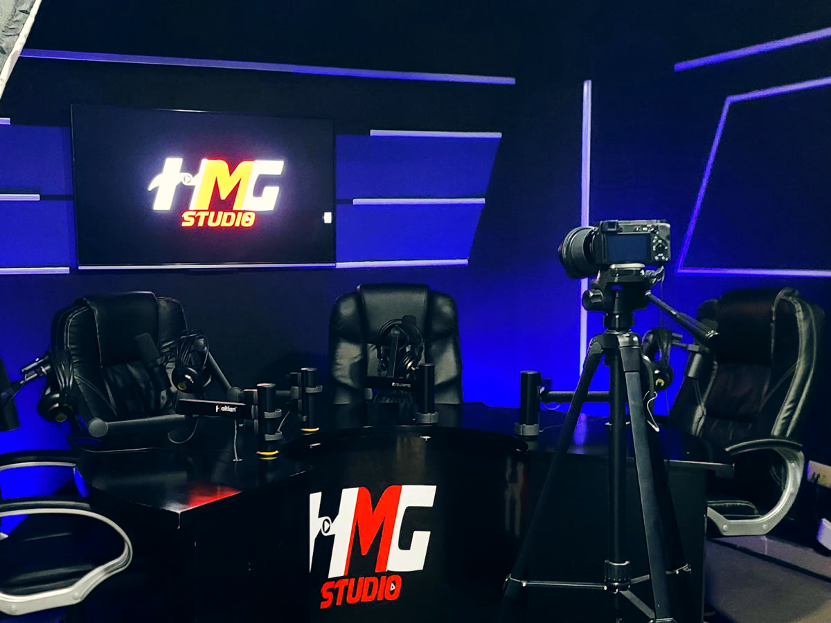 Set de grabación de HMG Studio con luces azules, pantalla con el logo y mesa para cuatro